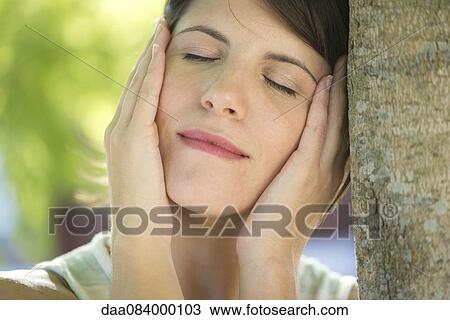 Woman leaning against tree trunk with hands on cheeks, eyes closed View Large Photo Image Stock Image - Woman leaning against tree trunk with hands on cheeks, eyes closed. Fotosearch