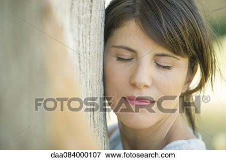 Woman leaning against tree trunk with eyes closed, portrait View Large Photo Image Stock Photo - Woman leaning against tree trunk with eyes closed, portrait. Fotosearch