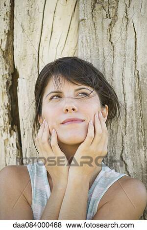 Woman leaning against tree trunk with face in hands, looking up dreamily View Large Photo Image Stock Photo - Woman leaning against tree trunk with face in hands, looking up dreamily. Fotosearch