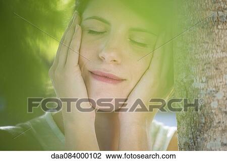 Woman leanng against tree trunk with hands on cheecks, eyes closed View Large Photo Image Stock Image - Woman leanng against tree trunk with hands on cheecks, eyes closed. Fotosearch
