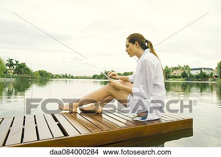 Woman relaxing on lake dock using digital tablet View Large Photo Image Picture - Woman relaxing on lake dock using digital tablet. Fotosearch
