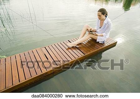 Woman relaxing on lake dock using digital tablet View Large Photo Image Stock Image - Woman relaxing on lake dock using digital tablet. Fotosearch