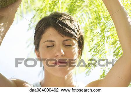 Stock Image - Woman shaded by foliage, eyes closed, portrait. Fotosearch