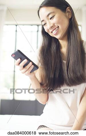 Woman sitting in bed using smartphone View Large Photo Image Stock Photo - Woman sitting in bed using smartphone. Fotosearch