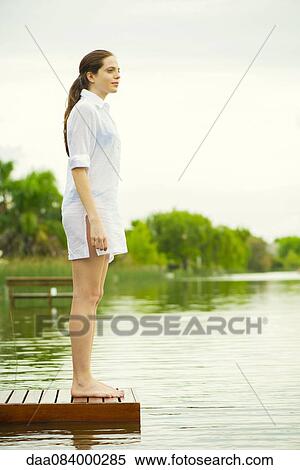 Stock Photography - Woman standing at end of lake dock looking at view. Fotosearch