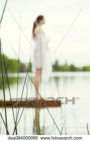 Woman standing at end of lake pier enjoying view, focus on tall grass in foreground View Large Photo Image Stock Image - Woman standing at end of lake pier enjoying view, focus on tall grass in foreground. Fotosearch