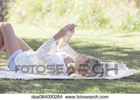 Woman streaming online video content on smartphone outdoors View Large Photo Image Picture - Woman streaming online video content on smartphone outdoors. Fotosearch