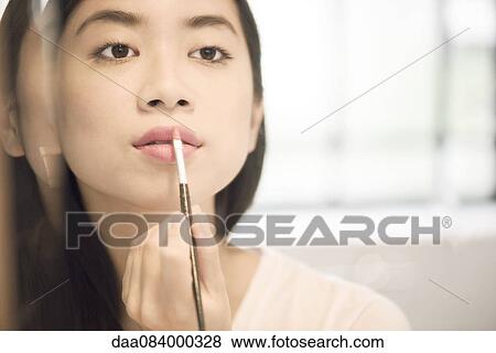 Stock Photo - Woman using lipbrush to apply lipstick. Fotosearch