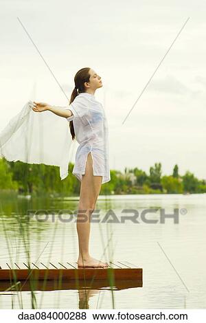 Woman with arms outstretched standing at end of lake pier View Large Photo Image Stock Photo - Woman with arms outstretched standing at end of lake pier. Fotosearch