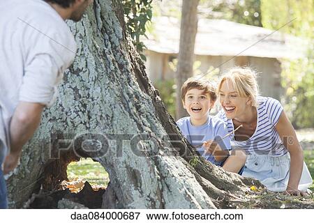Stock Photo - Young boy and mother hiding behind tree, playing hide-and-seek. Fotosearch