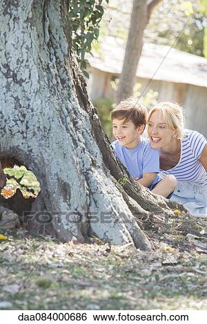Stock Photograph - Young boy and mother hiding behind tree, playing hide-and-seek. Fotosearch