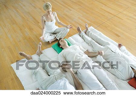 Stock Photography - Alternative therapy session, three adults lying side by side while therapist sits nearby. Fotosearch