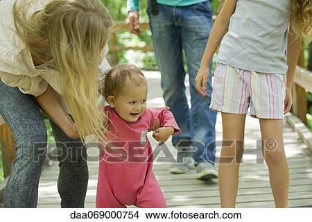 Baby girl learning to walk outdoors with family View Large Photo Image Picture - Baby girl learning to walk outdoors with family. Fotosearch