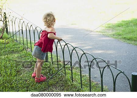 Stock Photography - Baby girl standing by fence. Fotosearch