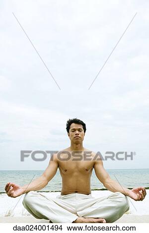 Barechested man sitting in lotus position, ocean in background View Large Photo Image Picture - Barechested man sitting in lotus position, ocean in background. Fotosearch