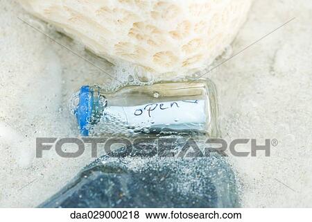 Bottle containing message in shallow water, close-up View Large Photo Image Stock Photo - Bottle containing message in shallow water, close-up. Fotosearch