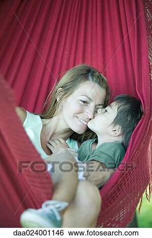 Stock Photograph - Boy and mother in hammock, boy kissing woman's face. Fotosearch