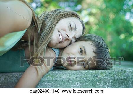 Stock Image - Boy and mother lying down, woman resting head on boy, boy smiling at camera. Fotosearch