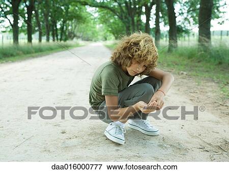Boy crouching in middle of dirt road, looking at pebbles View Large Photo Image Stock Photo - Boy crouching in middle of dirt road, looking at pebbles. Fotosearch
