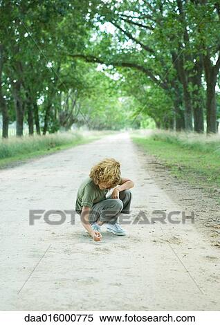 Stock Photography - Boy crouching in middle of dirt road. Fotosearch