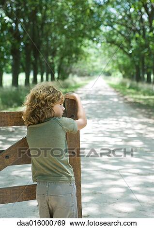 Boy leaning on gate, facing dirt road, rear view View Large Photo Image Stock Photo - Boy leaning on gate, facing dirt road, rear view. Fotosearch