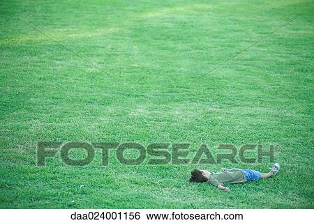 Stock Photograph - Boy lying in grass, high angle view, full length. Fotosearch