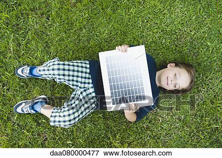 Boy lying on grass holding solar panel View Large Photo Image Stock Photo - Boy lying on grass holding solar panel. Fotosearch
