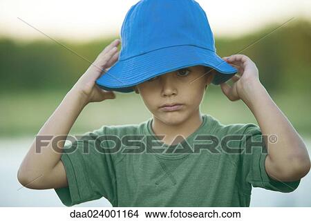 Picture - Boy putting on hat, head and shoulders. Fotosearch