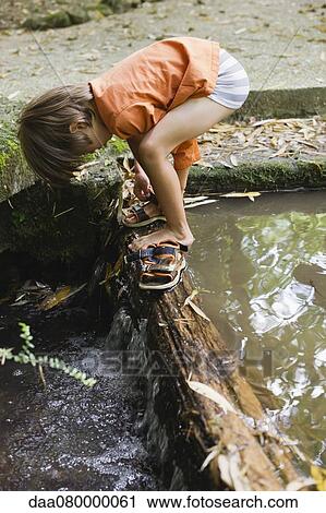 Boy putting on sandals by flowing water View Large Photo Image Stock Image - Boy putting on sandals by flowing water. Fotosearch