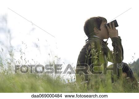 Boy sitting in field, looking through binoculars View Large Photo Image Picture - Boy sitting in field, looking through binoculars. Fotosearch