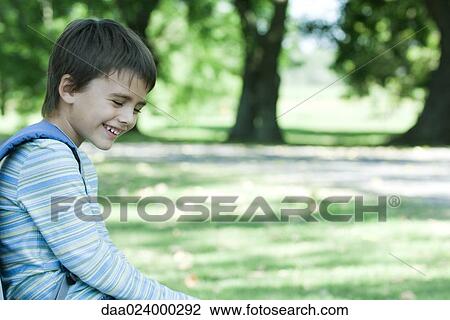 Stock Image - Boy sitting in park, laughing, side view. Fotosearch