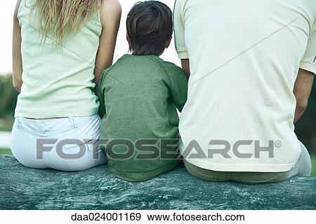 Boy sitting on log between parents, rear view, cropped View Large Photo Image Stock Photo - Boy sitting on log between parents, rear view, cropped. Fotosearch