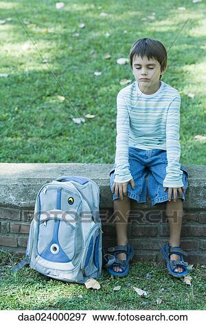 Boy sitting on low wall, backpack by side, eyes closed View Large Photo Image Stock Photo - Boy sitting on low wall, backpack by side, eyes closed. Fotosearch