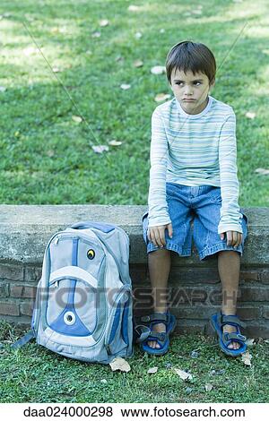 Boy sitting on low wall, backpack by side, looking away View Large Photo Image Stock Photo - Boy sitting on low wall, backpack by side, looking away. Fotosearch