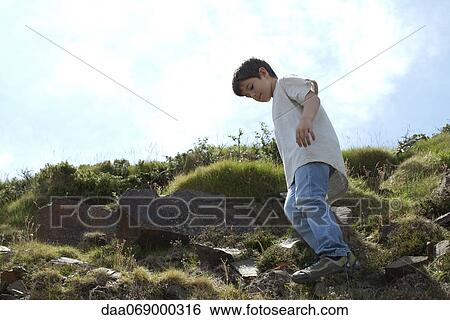 Stock Photograph - Boy standing on rocky hillside, low angle view. Fotosearch