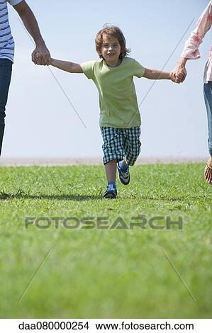 Picture - Boy walking hand in hand with parents outdoors, cropped. Fotosearch
