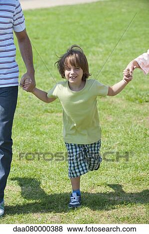 Stock Photo - Boy walking hand in hand with parents outdoors, cropped. Fotosearch