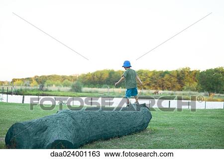 Stock Image - Boy walking on log, rear view. Fotosearch