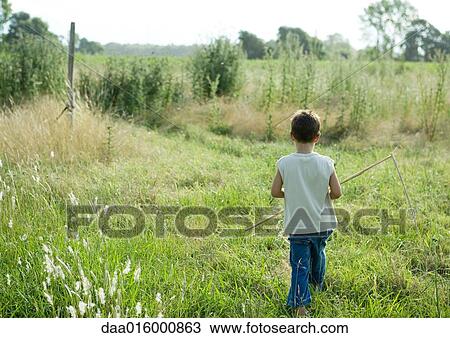 Stock Image - Boy walking through field, rear view. Fotosearch
