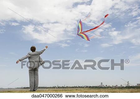 Businessman flying kite in field, rear view View Large Photo Image Stock Photograph - Businessman flying kite in field, rear view. Fotosearch