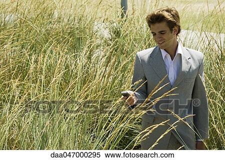 Stock Photography - Businessman in tall grass looking at cell phone. Fotosearch