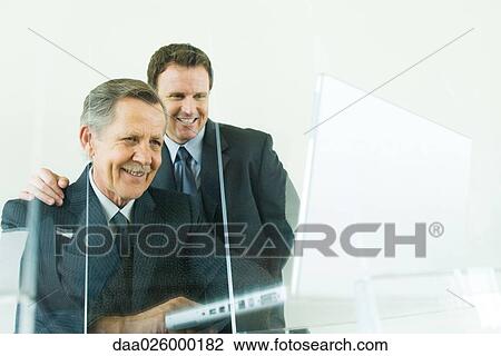 Stock Image - Businessman looking over colleague's shoulder at laptop computer, both smiling, low angle view. Fotosearch