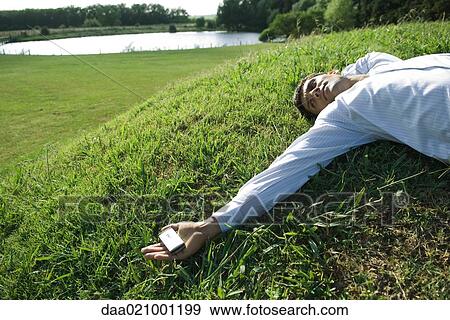 Businessman lying on grass, holding cell phone View Large Photo Image Stock Photo - Businessman lying on grass, holding cell phone. Fotosearch