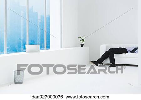 Businessman lying on sofa in minimalist high rise apartment, cropped view View Large Photo Image Stock Photograph - Businessman lying on sofa in minimalist high rise apartment, cropped view. Fotosearch