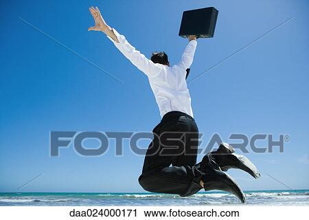 Businessman on beach, jumping into air with briefcase in hand View Large Photo Image Stock Image - Businessman on beach, jumping into air with briefcase in hand. Fotosearch