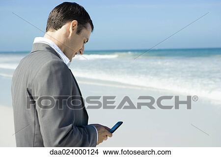 Picture - Businessman on beach, using cell phone. Fotosearch