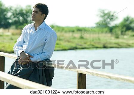 Picture - Businessman on wooden footbridge over lake, looking away. Fotosearch