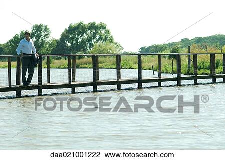 Businessman on wooden footbridge over lake, looking away View Large Photo Image Stock Image - Businessman on wooden footbridge over lake, looking away. Fotosearch