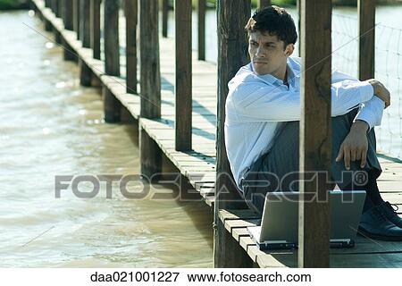 Businessman on wooden footbridge over lake with laptop, looking away View Large Photo Image Stock Photo - Businessman on wooden footbridge over lake with laptop, looking away. Fotosearch