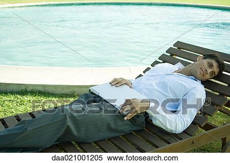 Businessman reclining in lounge chair near pool, holding laptop on lap View Large Photo Image Stock Photography - Businessman reclining in lounge chair near pool, holding laptop on lap. Fotosearch